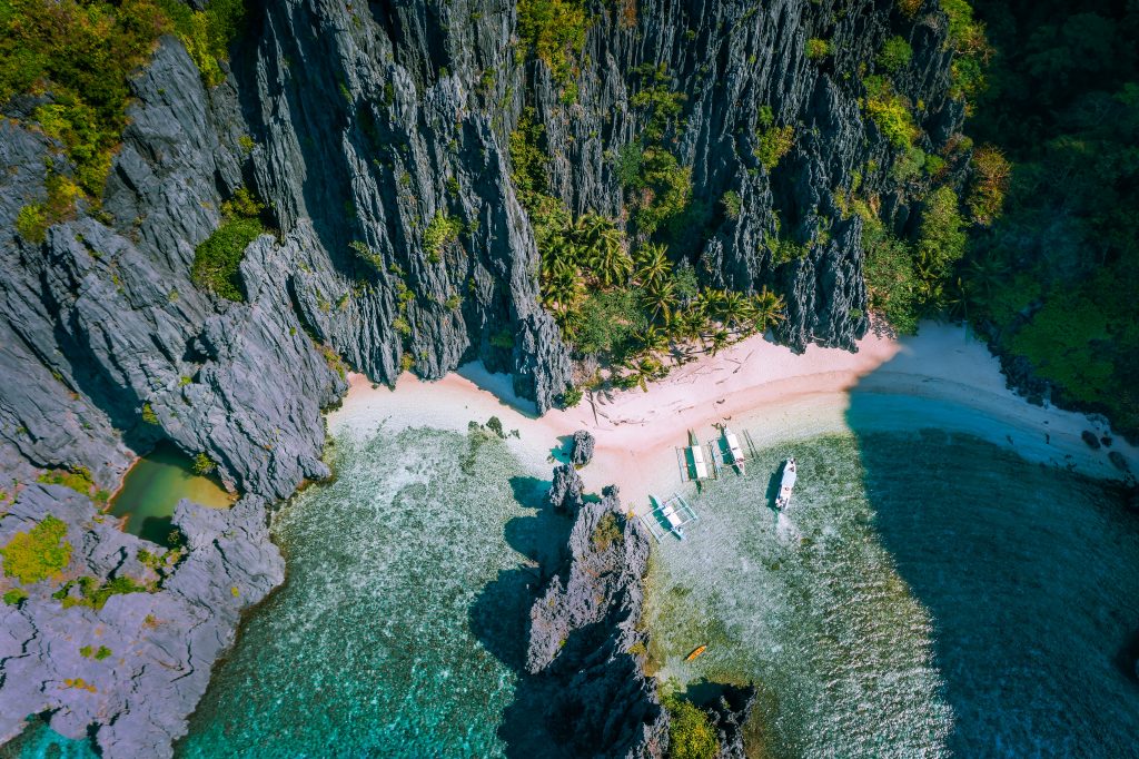 El Nido, Palawan, Philippines. Aerial view of Secret hidden lagoon beach with tourist banca boats on island hopping tour surrounded by karst cliffs scenery
