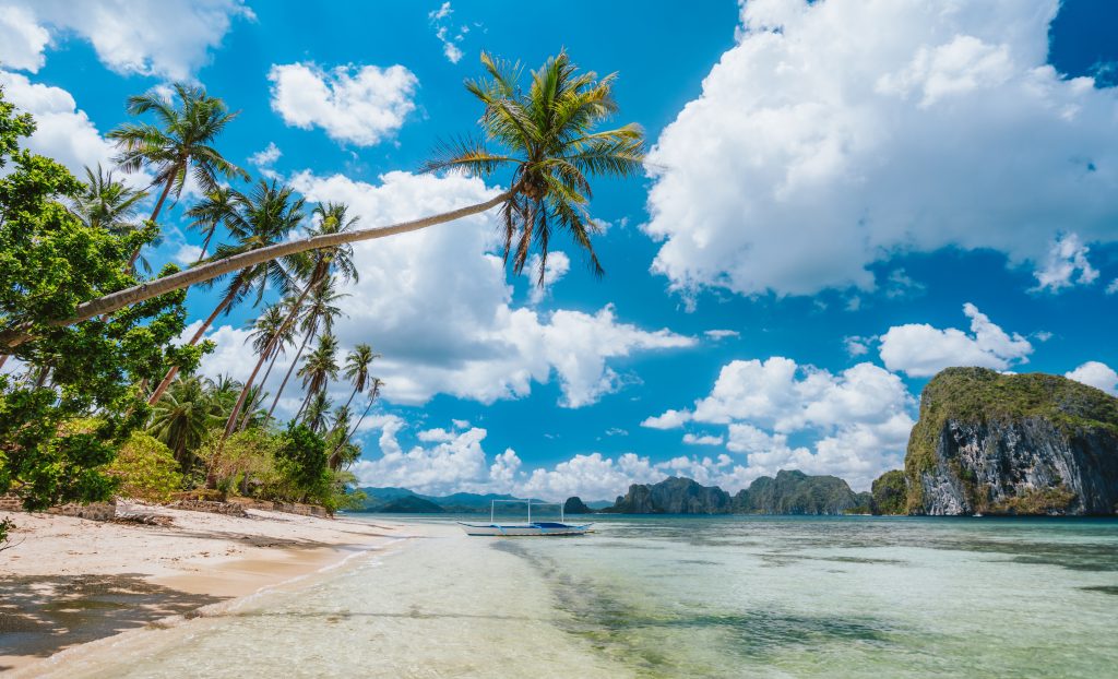 El Nido, Palawan, Philippines. Exotic beach with palm trees, tourist boat on the sandy beach and blue sky with white clouds